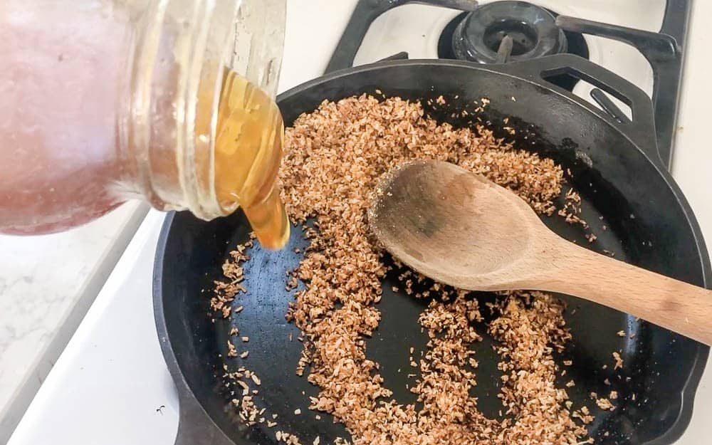 honey in a mason jar being poured onto toasted coconut flakes in a cast iron skillet