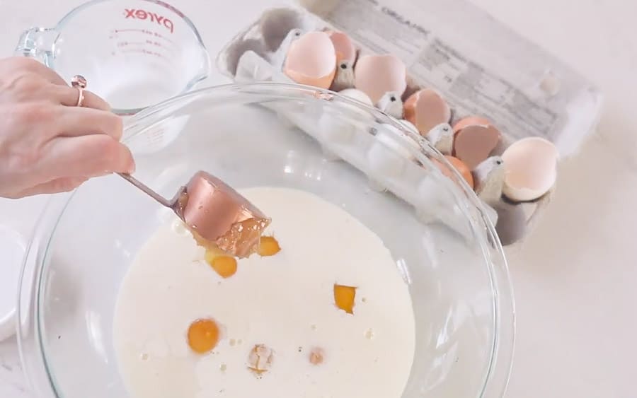 adding eggs, milk, honey, and other ingredients to a glass bowl to make sourdough French toast