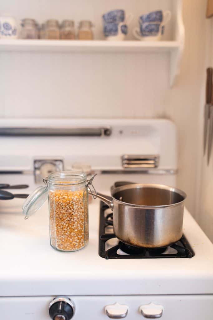 stainless steel pot on the stove with a jar of popcorn kernels to the left