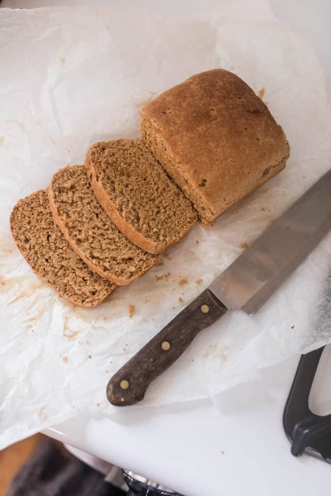 einkorn bread sliced on parchment paper with a knife next to it.