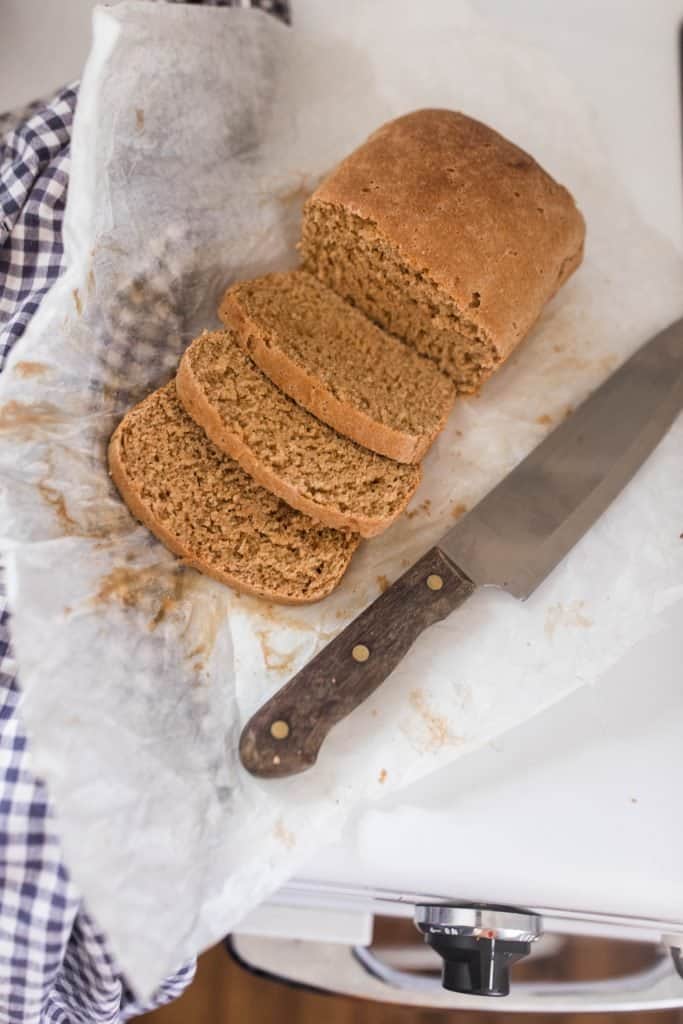 overhead shot of sliced einkorn sandwich break on parchment paper. A knife lays to the right and a checked towel to the left