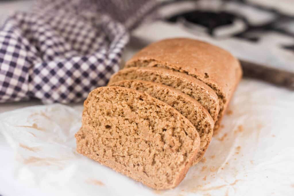 einkorn sandwich bread sliced on a stove top with a blue and white checked towel in the background