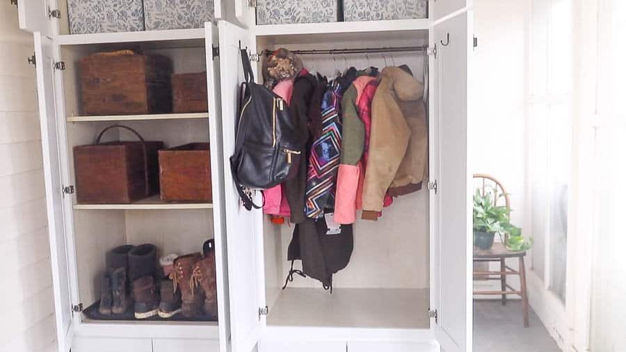 farmhouse mud room organization with coats hanging on one side and bins on the other