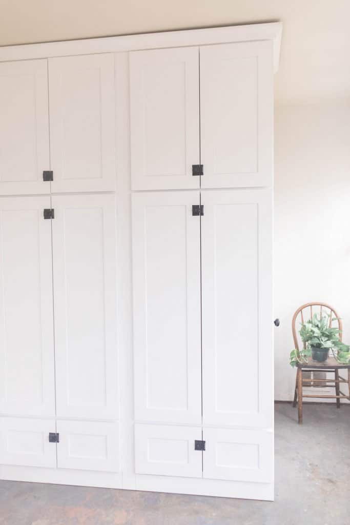 farmhouse mudroom with large white cabinets with black latches, gray painted floors, and a chair with a plant in the background