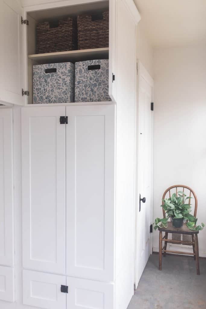 large white cabinet with bin organization. A chair with a plant to the right