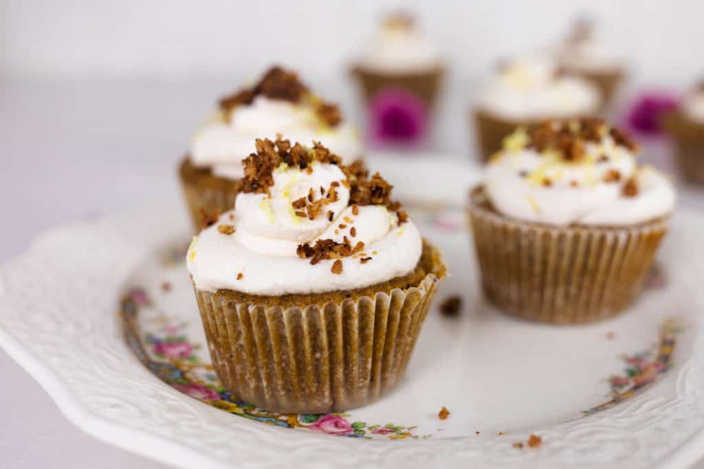 three muffins topped with frosting, lemon zest and toasted coconut on a antique plate