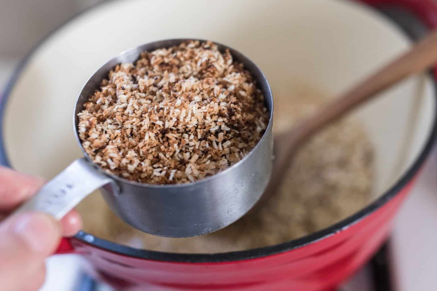 toasted coconut in a cup measuring cup over pot.