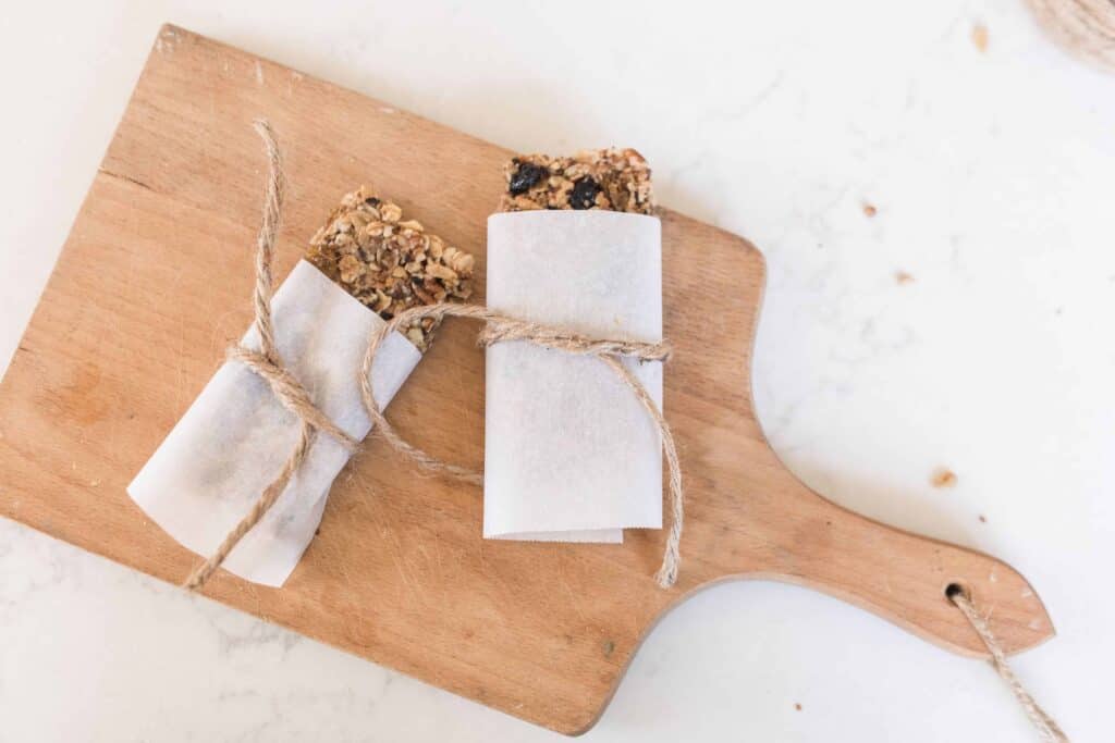 two gluten free granola bars wrapped with parchment paper and tied with twine on a wood cutting board on a quarts countertop