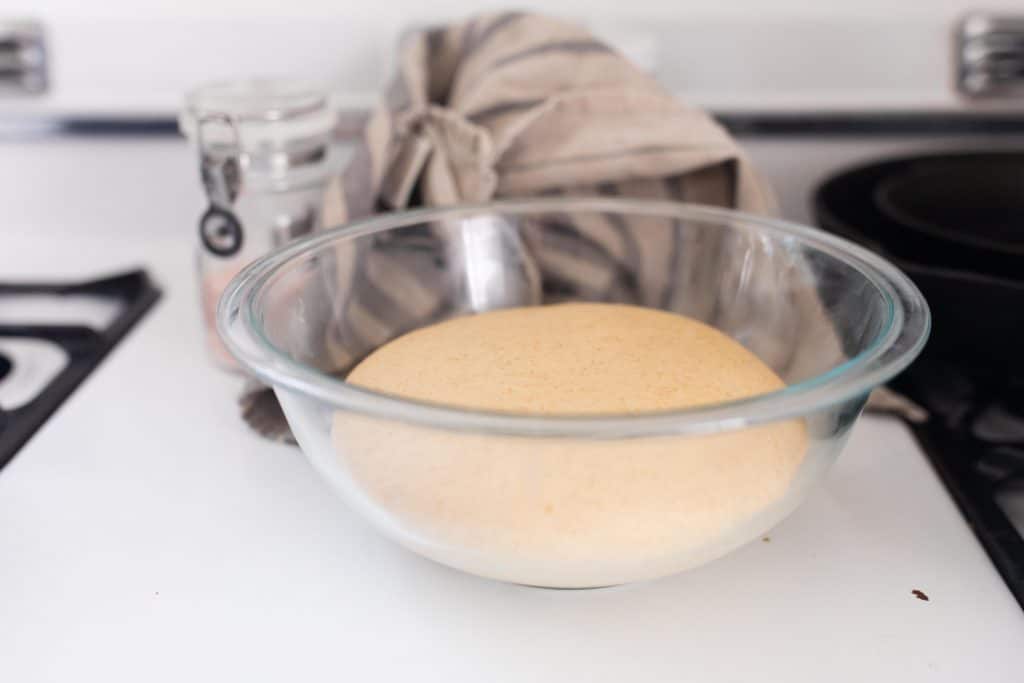 risen sourdough dinner roll dough in a glass bowl.
