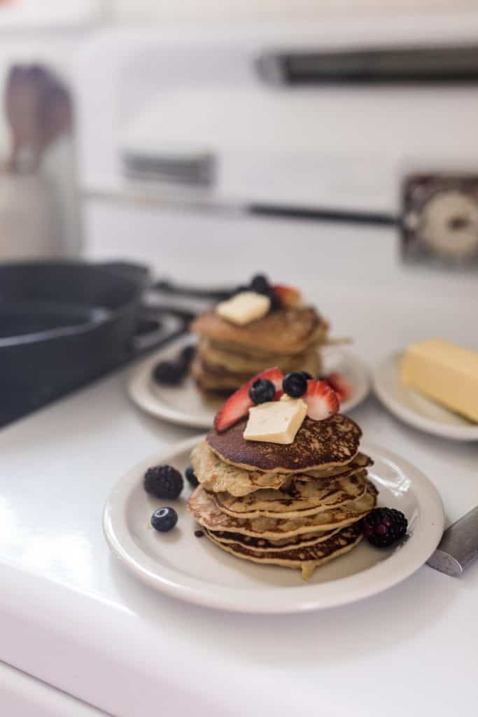 two plates full of sourdough gluten free pancakes with butter, strawberries, and blueberries on top.