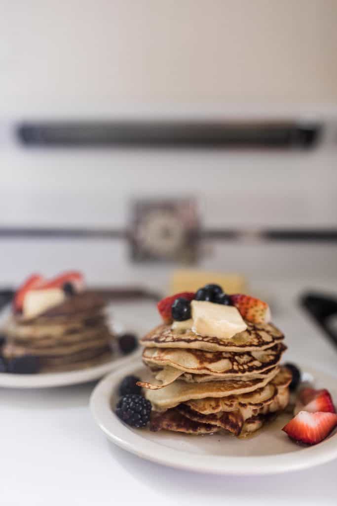 two white plates stacked with sourdough buckwheat pancakes and topped with butter and fresh berries