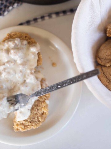 sourdough biscuits smothered in sausage gravy on a white plate. A bowl of sourdough biscuits to the right