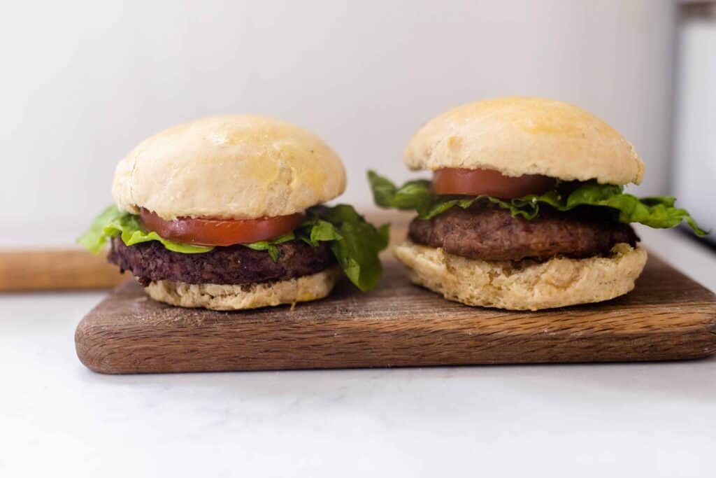 two burgers with tomato and lettuce on homemade sourdough buns on a cutting board