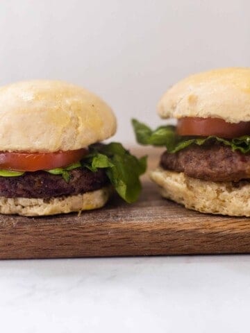two burgers with tomato and lettuce on homemade sourdough buns on a cutting board