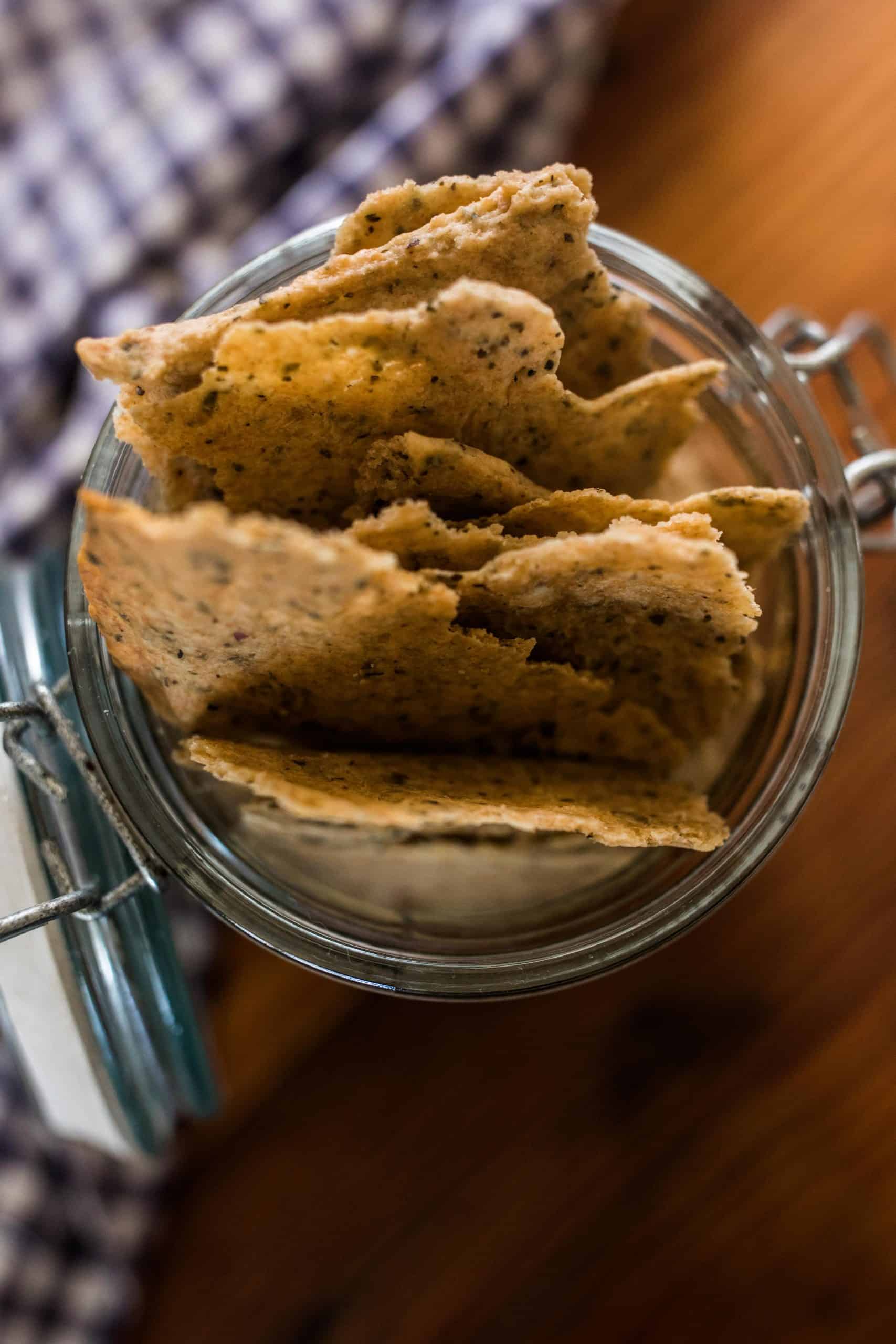 overhead shot of crispy sourdough crackers in a glass mason jar with a blue and white checked towel