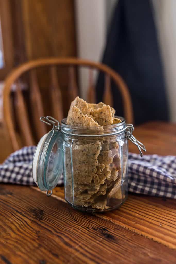 whole wheat crackers in a glass mason jar with a swing top lid on a wood table with a blue and white towel and chair in the background