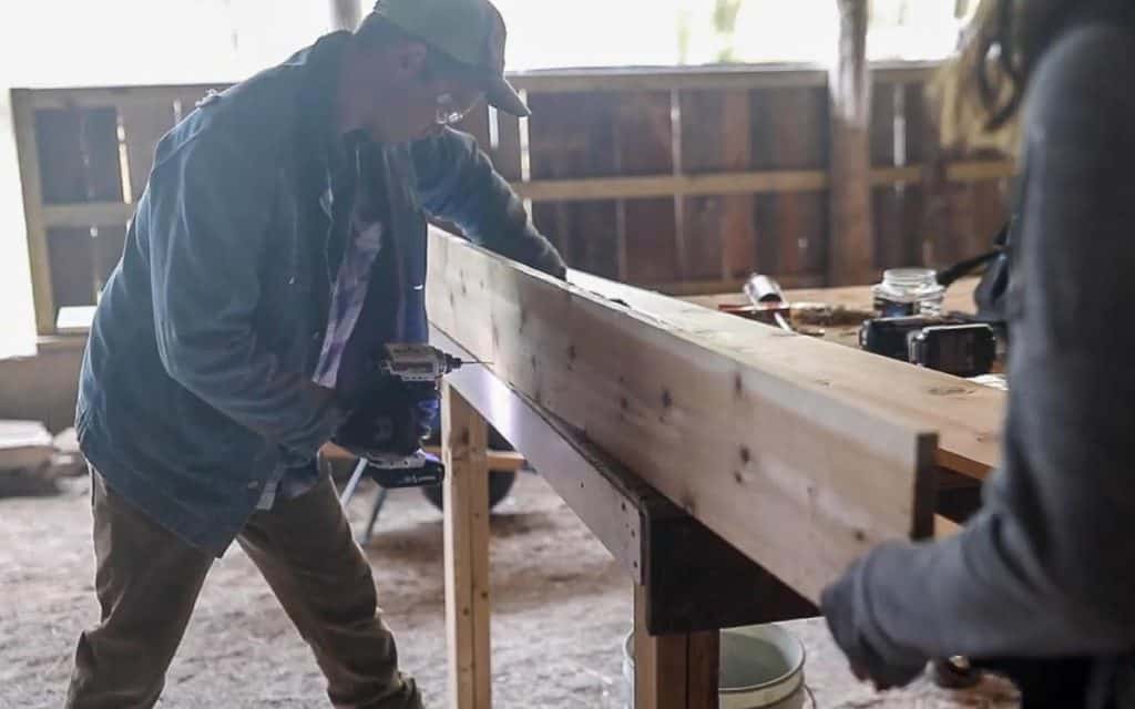 man nailing a board to a bottom board to create a box