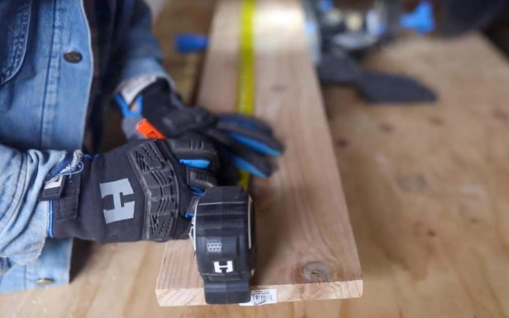 man wearing gloves measuring a pine board with a measuring tape