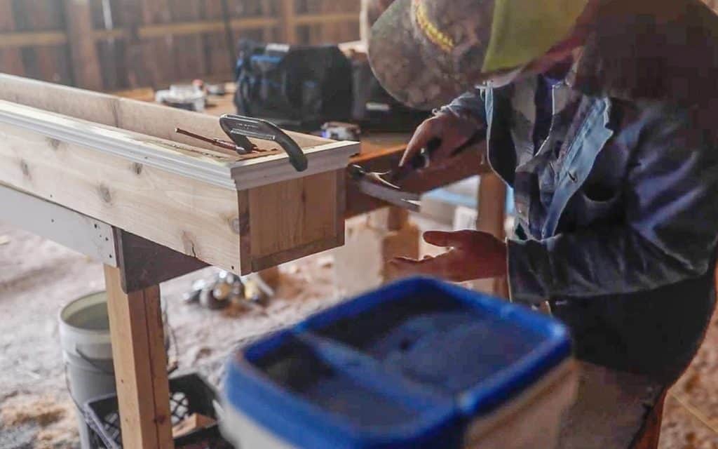 man hammering decorative trim on a diy window box using finishing nails