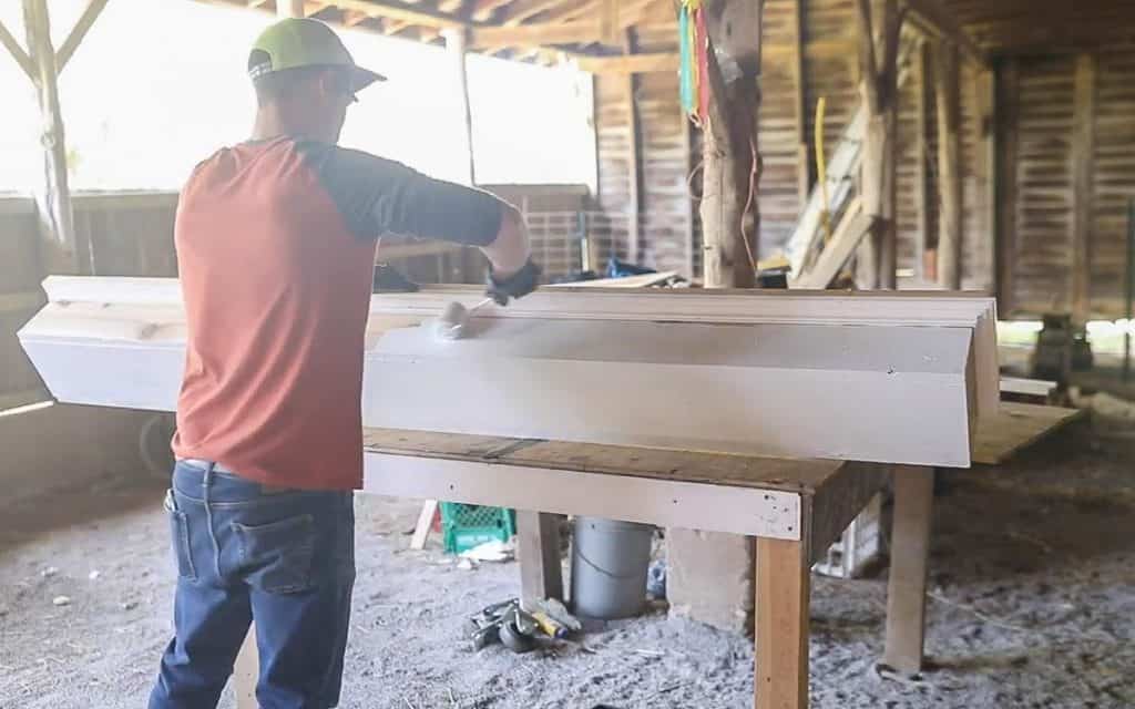 a man wearing an orange and blue shirt painting a DIY window box white with a roller