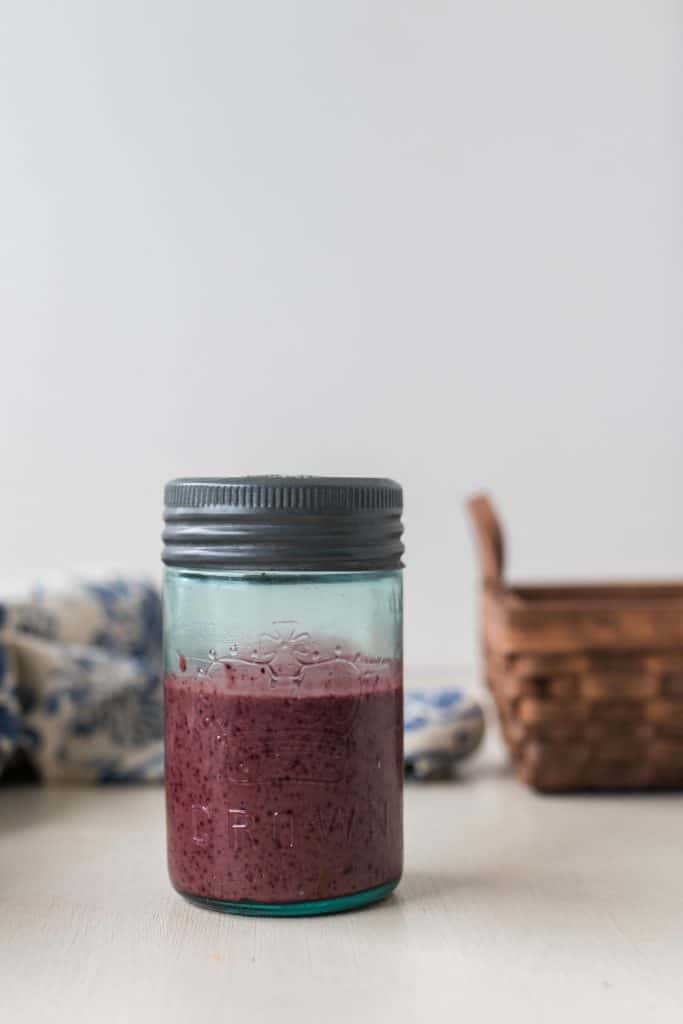 Fermented Blueberry Balsamic Dressing in a glass jar with a tin lid, basic and towel in the background