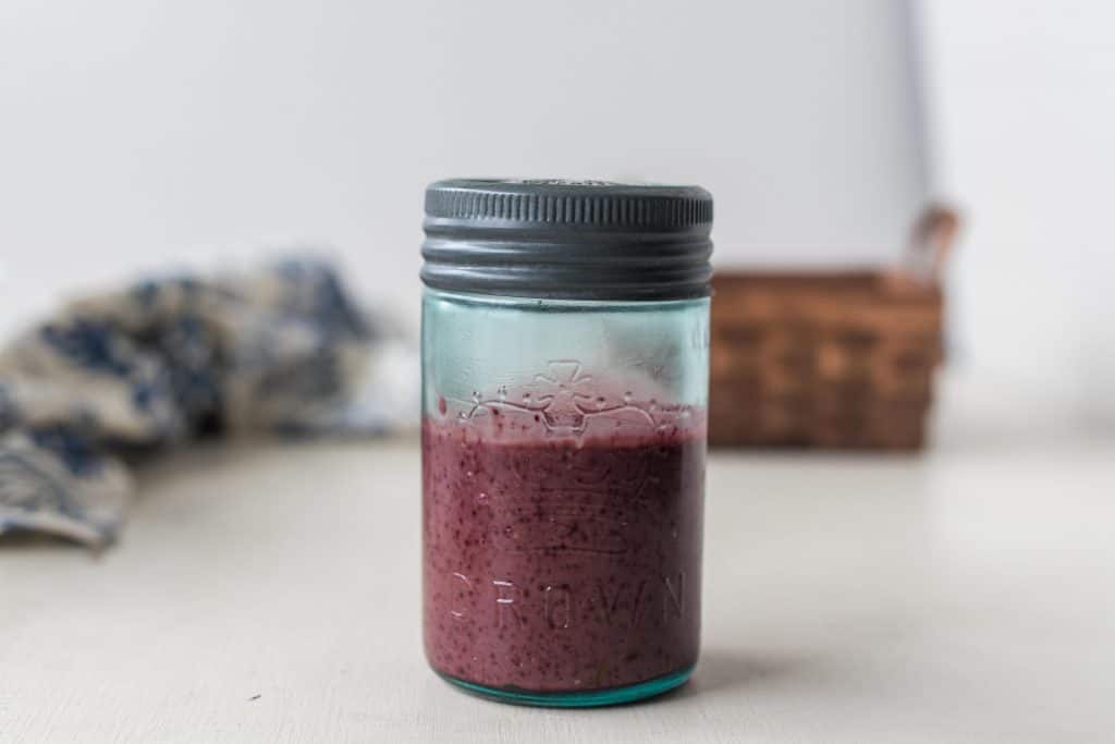 fermented balsamic blueberry vinaigrette dressing in a glass jar with metal lid, a woven basket and blue and white towel in the background