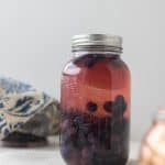 fermented fruit in a large mason jar with a silver bowl covered with a white and blue damask napkin in the background