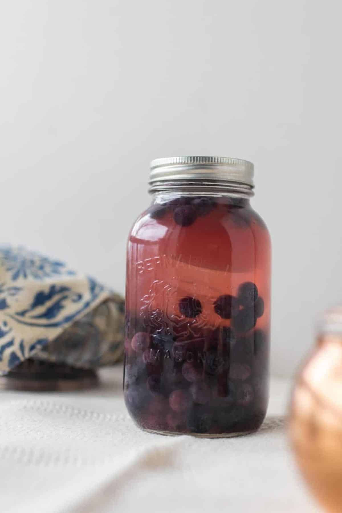 A mason jar with fermented blueberries on a white tablecloth. 