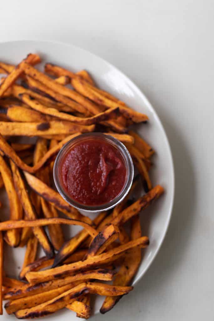 jar of homemade fermented ketchup on a white plate covered with sweet potato fries