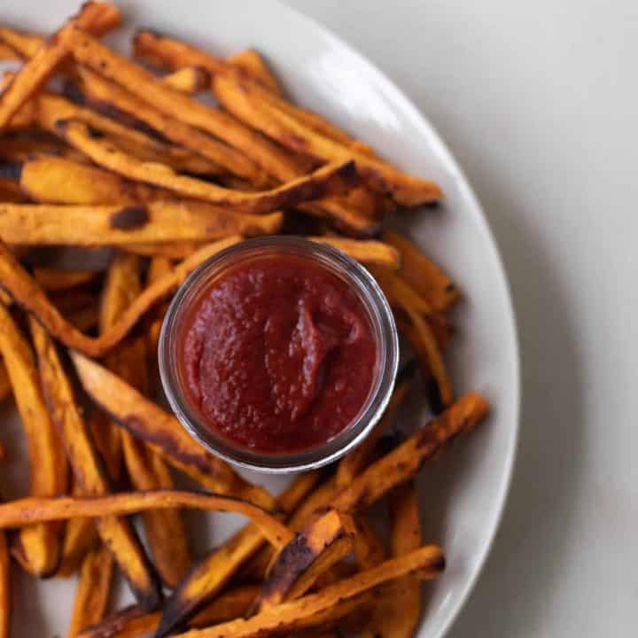 jar of homemade fermented ketchup on a white plate covered with sweet potato fries