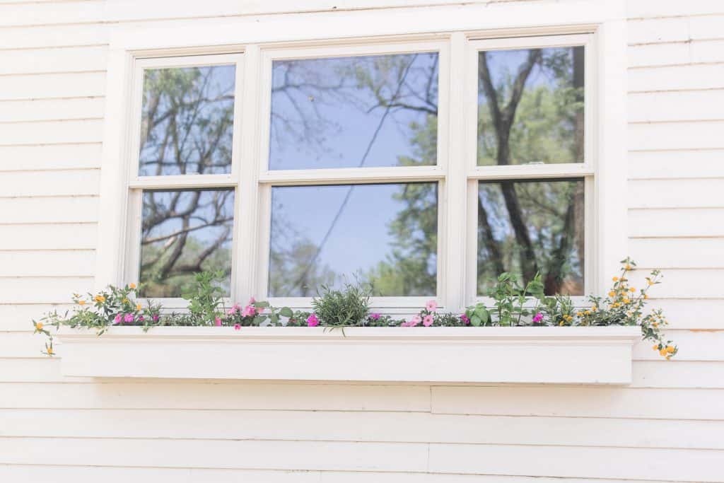 a white diy window box hanging below a window with yellow and pink flowers