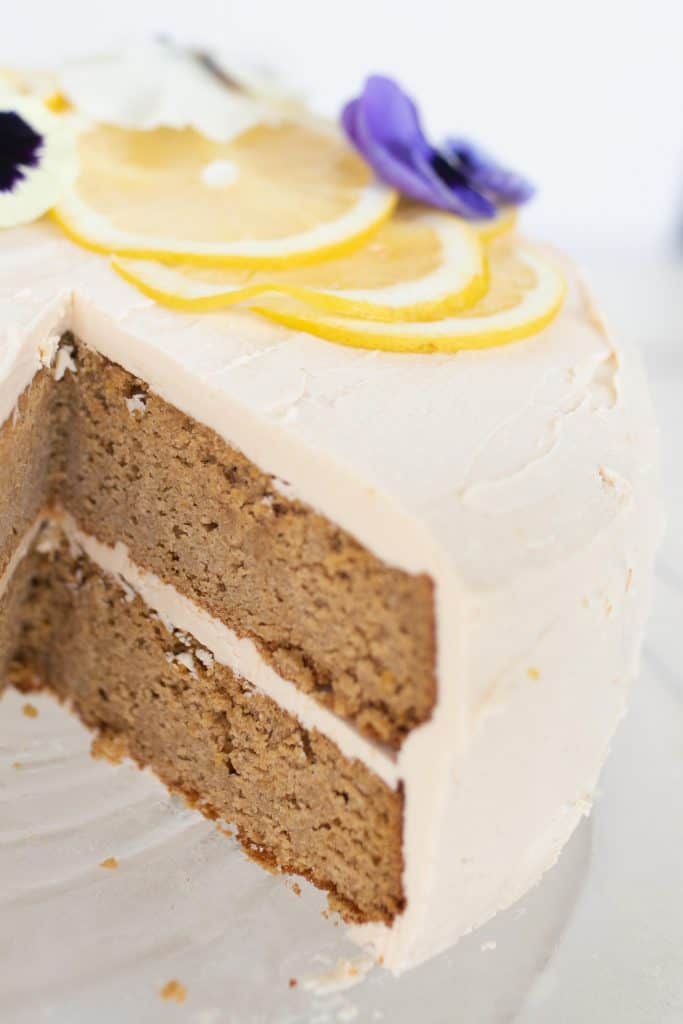 close up picture of a two tiered gluten free lemon cake with earl grey and lemon icing with a slice taken out. The cake is topped with lemon slices and edible flowers