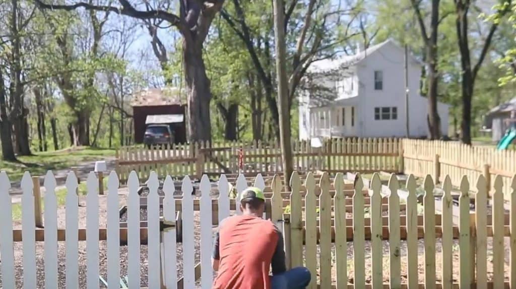 man wearing red shirt in painting a diy picket fence white with a roller