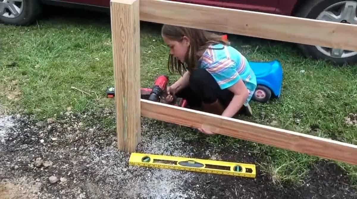 girl screwing in fence stringers onto post