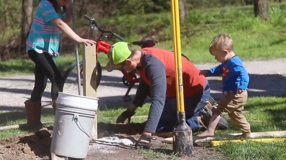 man adding screening gravel to a hole to place fence posts. Girl holding fence post level