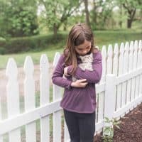 girl wearing a purple shirt cuddling a kitten in front of a DIY picket fence