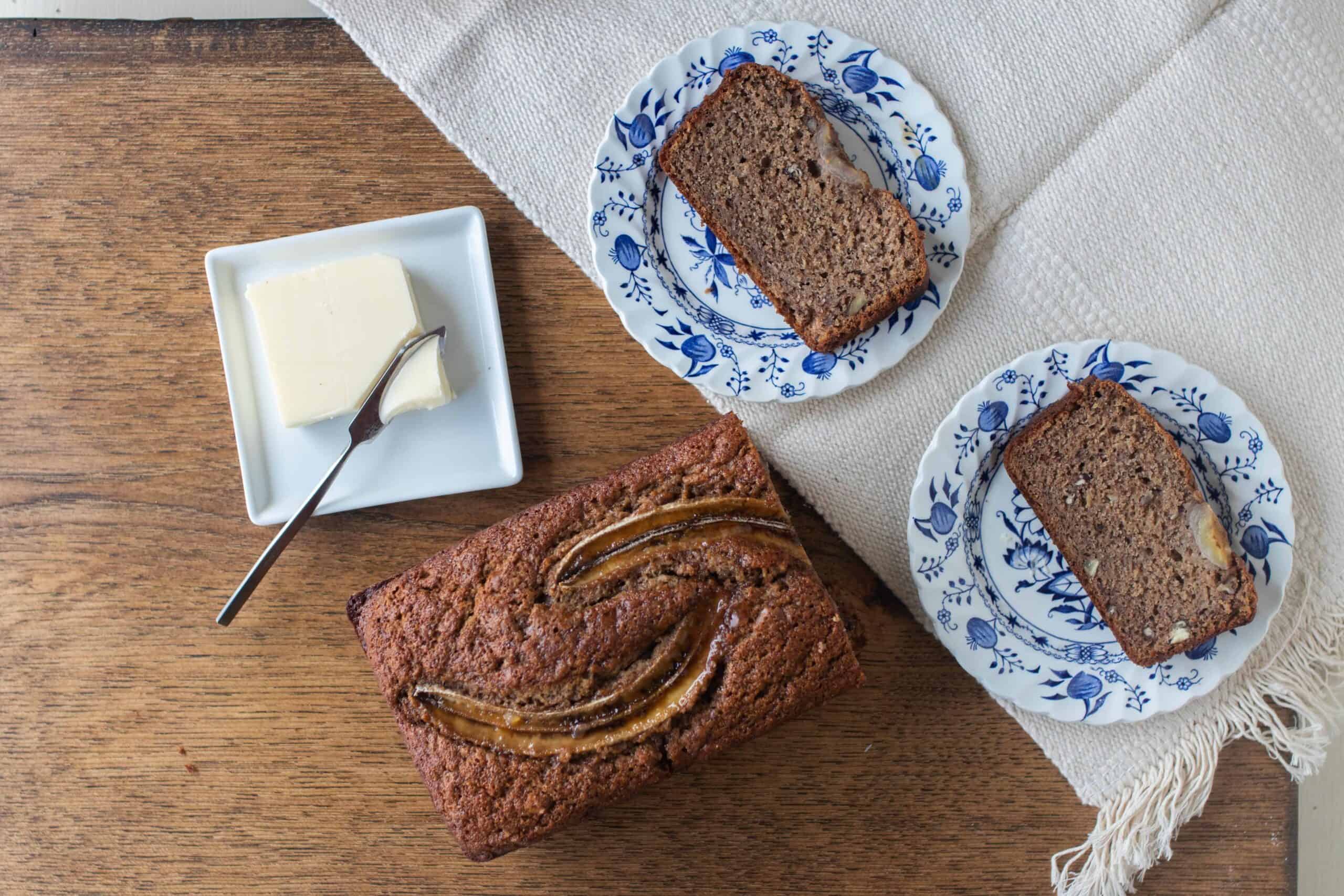 half loaf of sourdough banana bread on a table with two blue and white plates with slices of banana bread.
