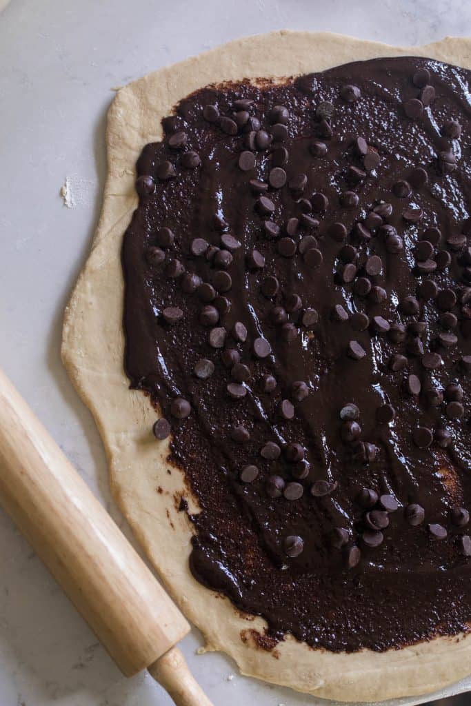 butter, sugar, and cocoa powder filling spread out on rolled out dough. Chocolate chips sprinkled on top