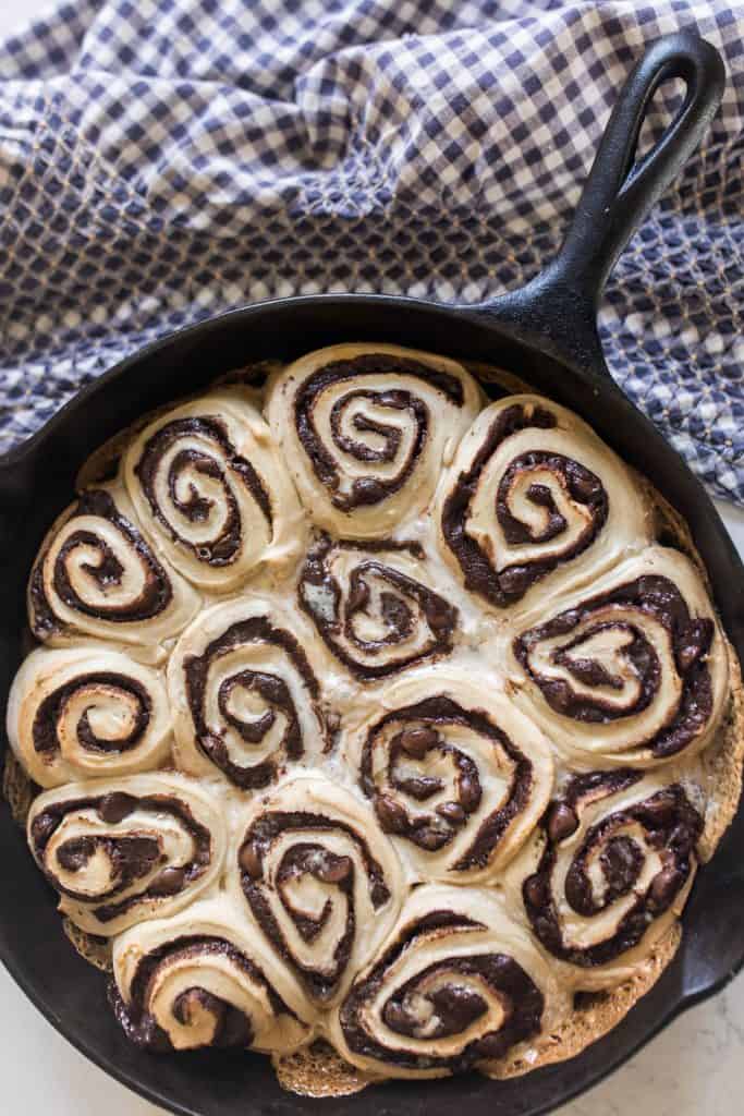 sourdough chocolate rolls in a cast iron skillet on a white and blue checked towel