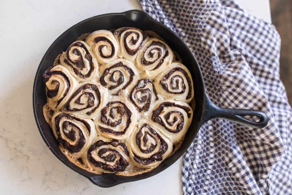 sourdough chocolate rolls in a cast iron skillet with a blue and white checked towel to the right
