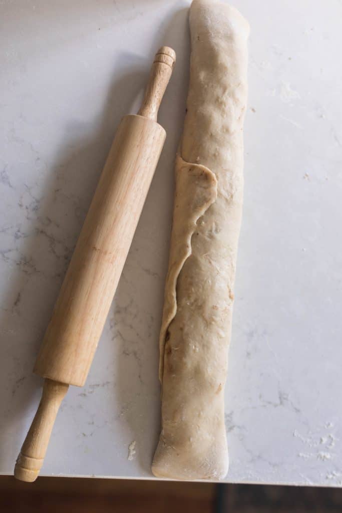 sourdough chocolate roll dough rolled up tight and ready to be sliced. a rolling pin rests to the left