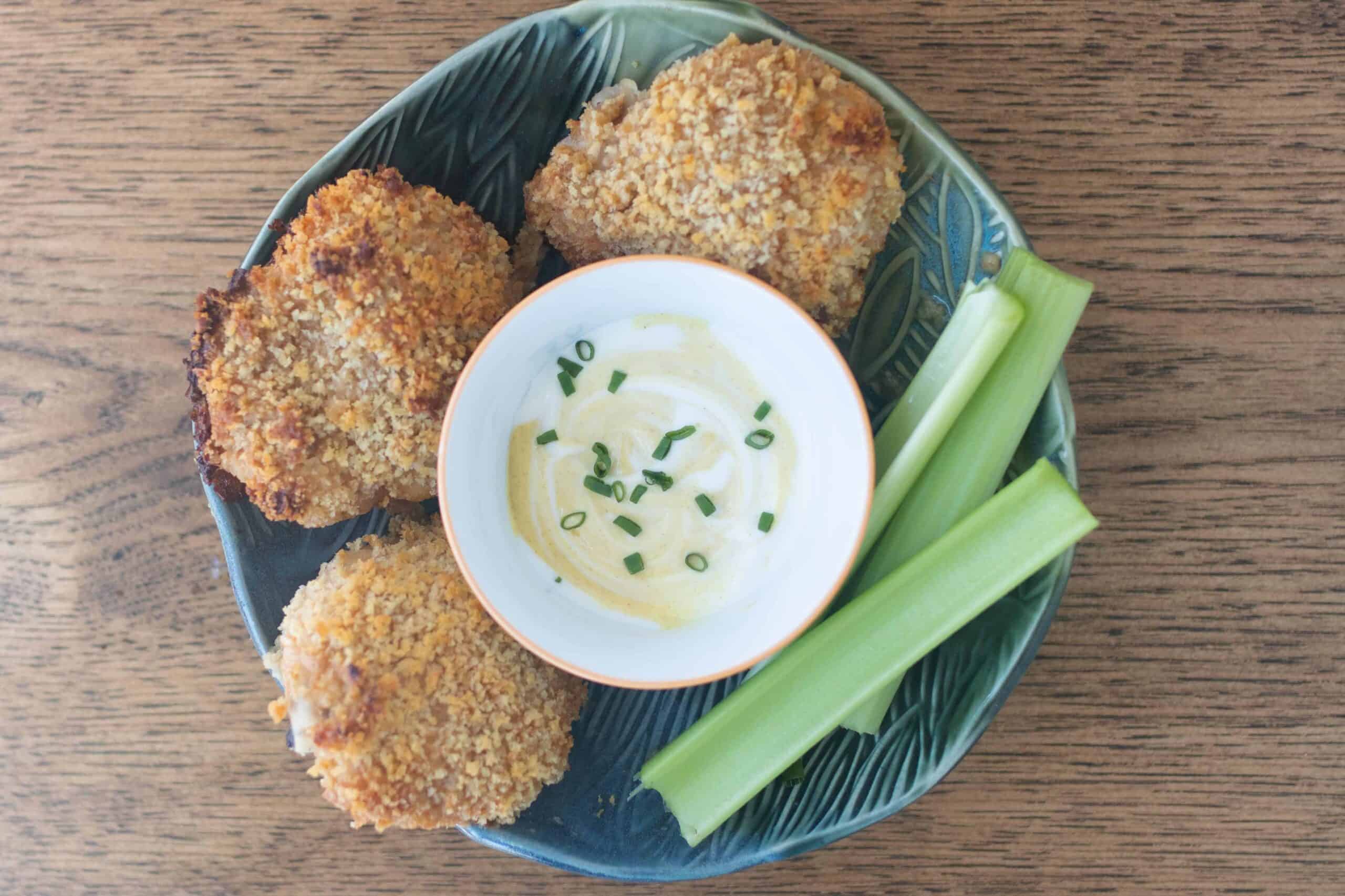 three sourdough fried chicken thighs in a tin bowl with a small bowl of mustard dipping sauce and celery sticks to the right
