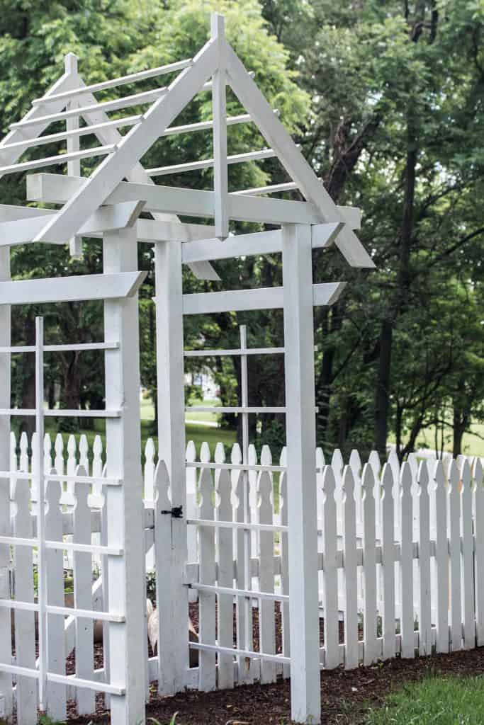 white arbor next to a white picket fence going into a garden