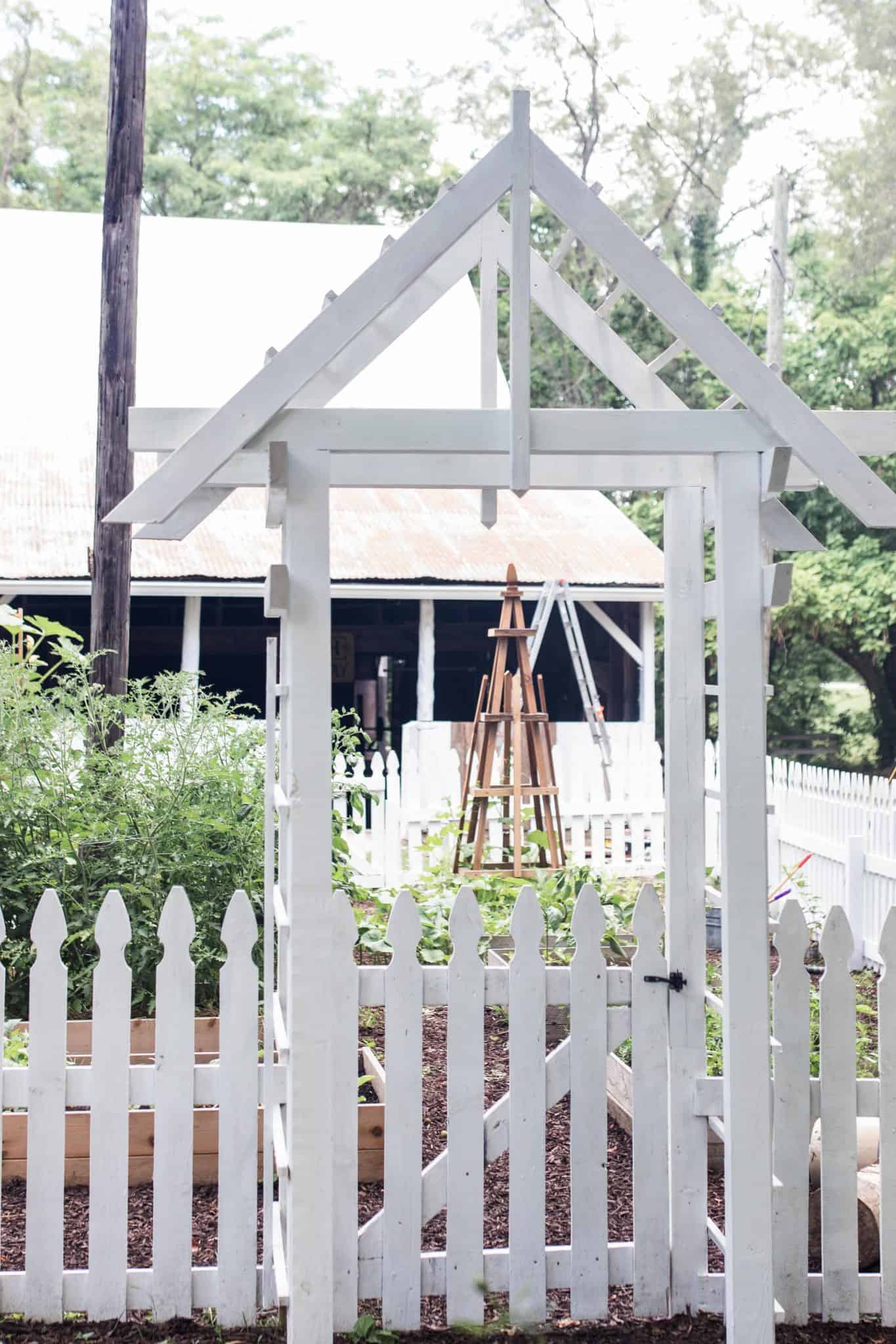 white arbor with a white picket fence into a garden