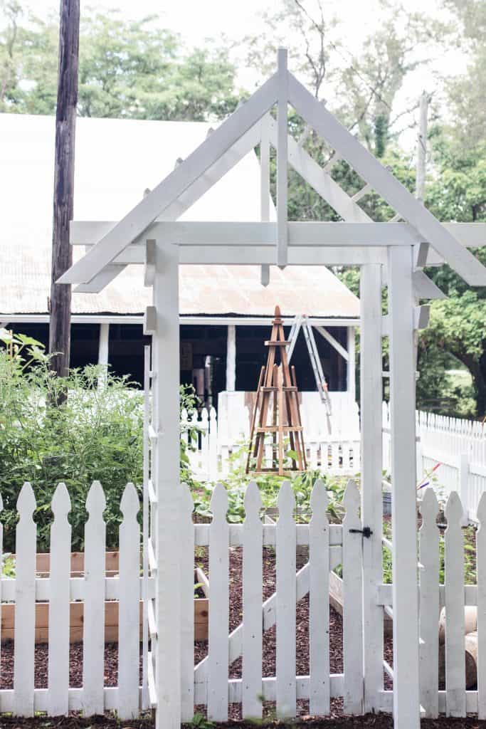 white arbor with a white picket fence into a garden 