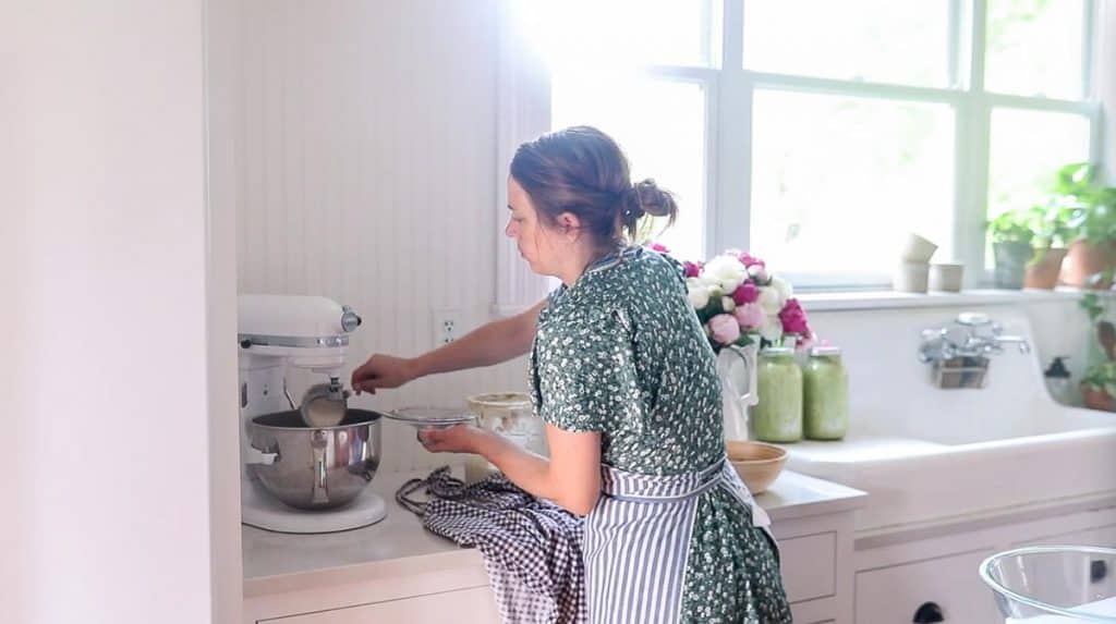 women wearing floral dress adding sourdough starter to a stand mixer to make artisan bread