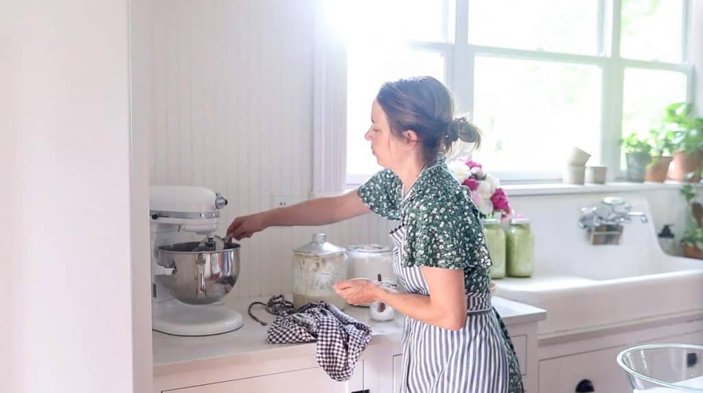 women wearing floral dress adding flour to a stand mixer to make artisan bread
