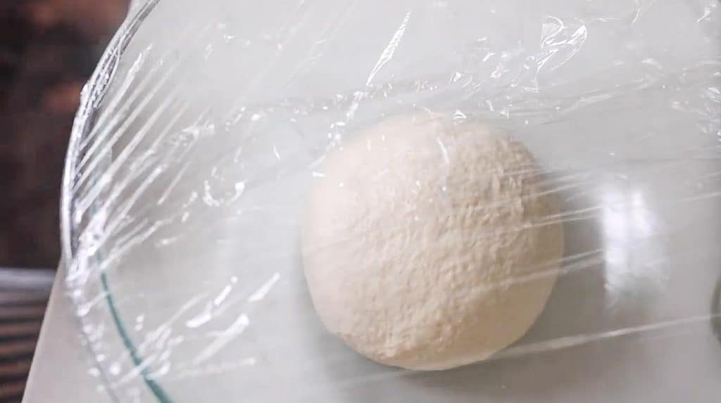 ball of dough in a greased glass bowl covered in plastic wrap