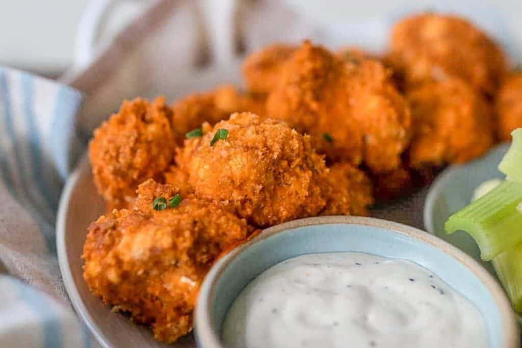 close up picture of buffalo cauliflower bites in a gray plate with dipping sauce
