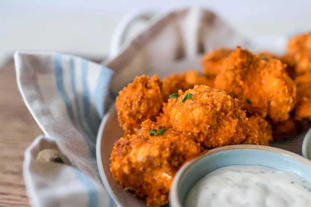 sourdough battered buffalo cauliflower wings in a tray with dippings sauce. Plate is on a blue and cream napkin